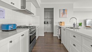 A modern kitchen with white cabinets, a blue toaster, a stove, and a microwave. - StayAU Contemporary 5BRM Families Home Point Cook (Point Cook)
