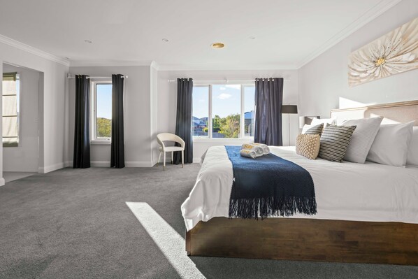 A modern bedroom with a large bed, dark curtains, a view of the outdoors, and a white chair. - StayAU Contemporary 5BRM Families Home Point Cook (Point Cook)