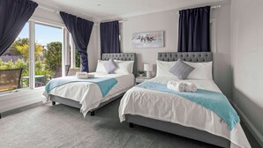 A hotel room with two beds, a window with curtains, a cityscape painting, and a view of greenery outside. - StayAU Contemporary 5BRM Families Home Point Cook (Point Cook)