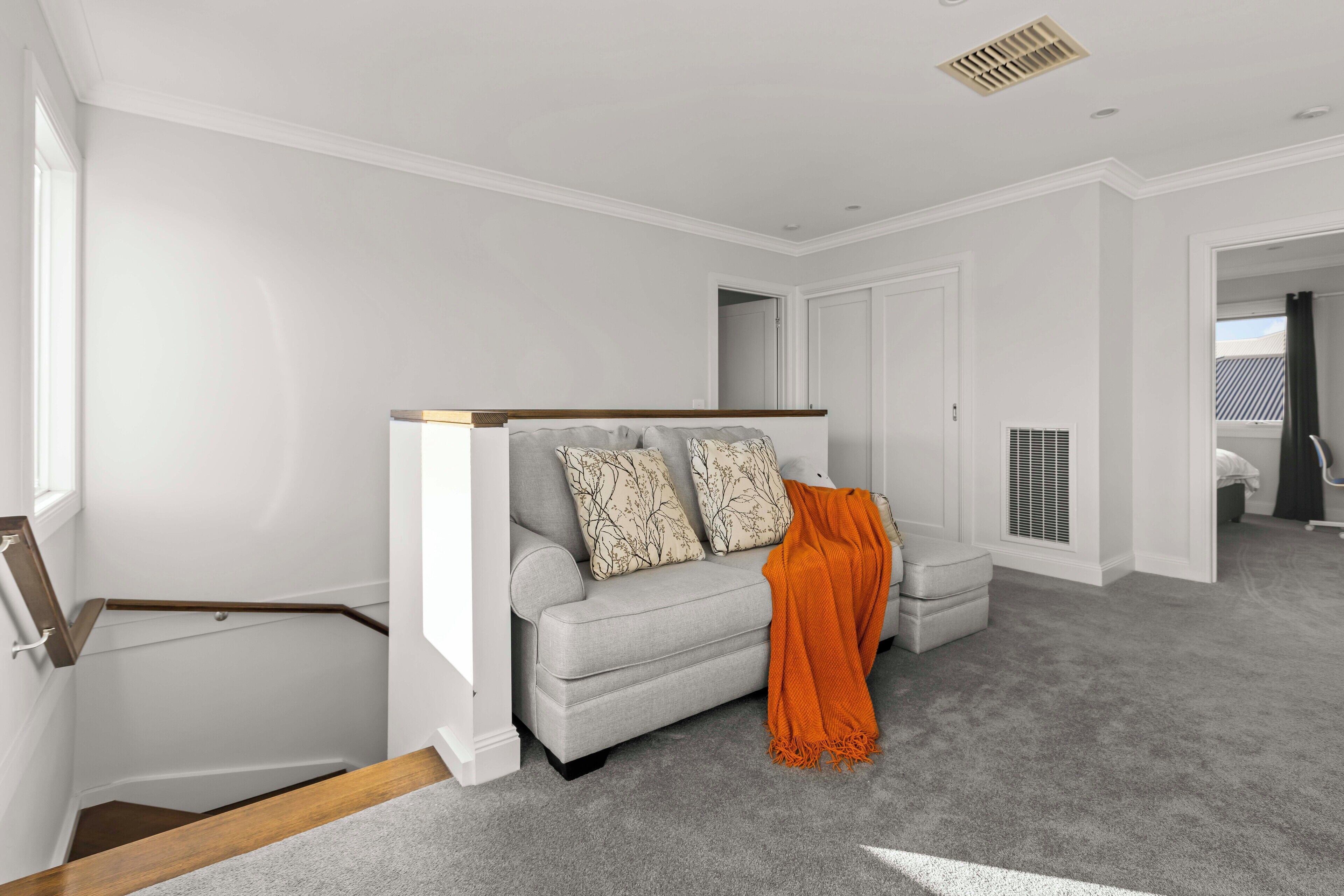 Un salon moderne avec un canapé gris, deux coussins à motifs et un plaid orange.