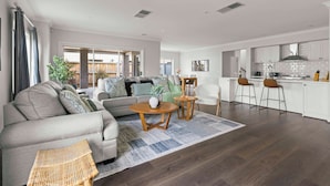 A spacious living area with a sofa, coffee table, and chairs, a kitchen with white cabinets, and a large window. - StayAU Contemporary 5BRM Families Home Point Cook (Point Cook)