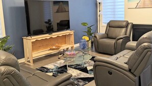 A modern living room with a flat-screen TV on a wooden stand, leather sofas, a glass coffee table, and a fireplace.