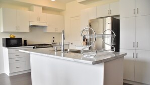 A modern kitchen with white cabinetry, a stainless steel refrigerator, a built-in microwave, and a marble countertop.