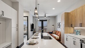 A modern kitchen with a central island, white cabinetry, and a wooden accent wall. - Luxury King Bed+Pool+Gym+DowntownATX+Domain+Q2Stadium (Austin)