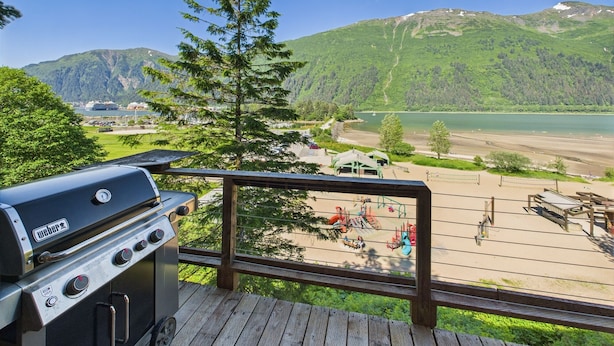 A deck with a Weber grill overlooking a lake and mountains.
