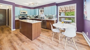 A modern kitchen with a central island, wooden cabinets, and a dining area with white chairs.