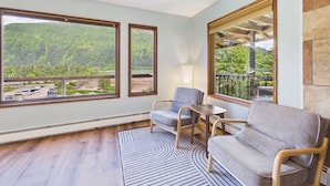 A room with large windows, a sofa, a chair, a small table, and a lamp.