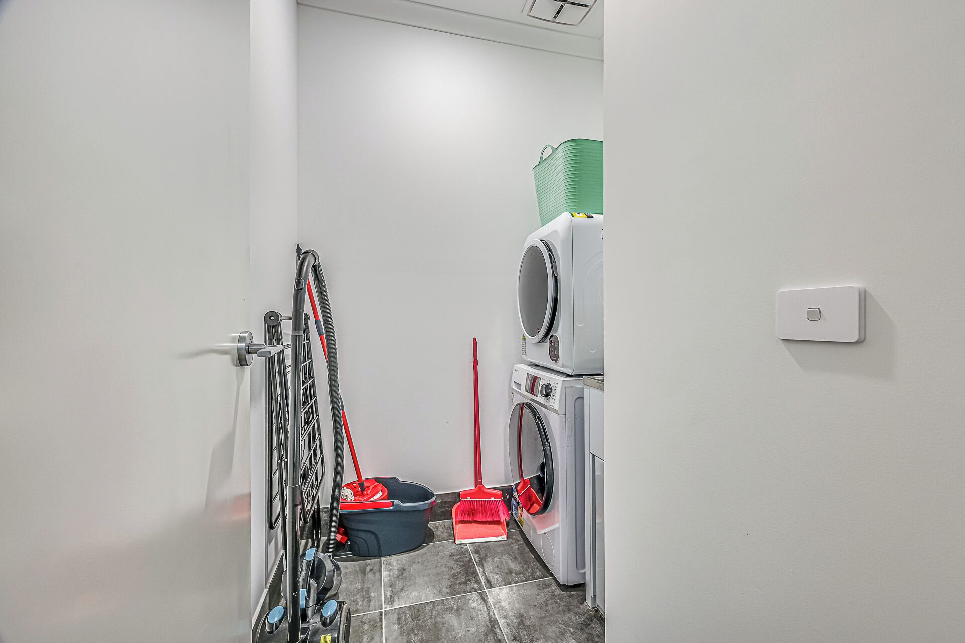 A laundry area with stacked washing machines, a mop, and a broom.