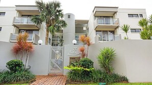 A modern apartment building with balconies, a central entrance gate, and well-maintained landscaping. - Beachfront Location -Ground Floor. Listen to the waves! (Mooloolaba)