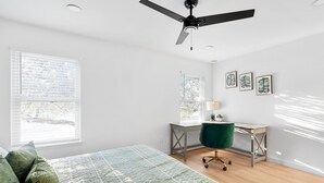 Ein Schlafzimmer mit Bett, Schreibtisch, Stuhl und Deckenventilator.