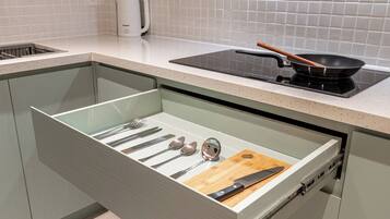 A kitchen with a drawer containing utensils, a cutting board, and a frying pan on a stove.