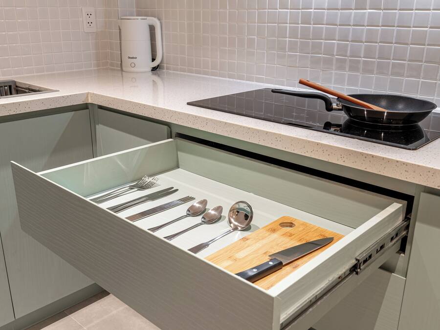 A kitchen with a drawer containing utensils, a cutting board, and a frying pan on a stove.