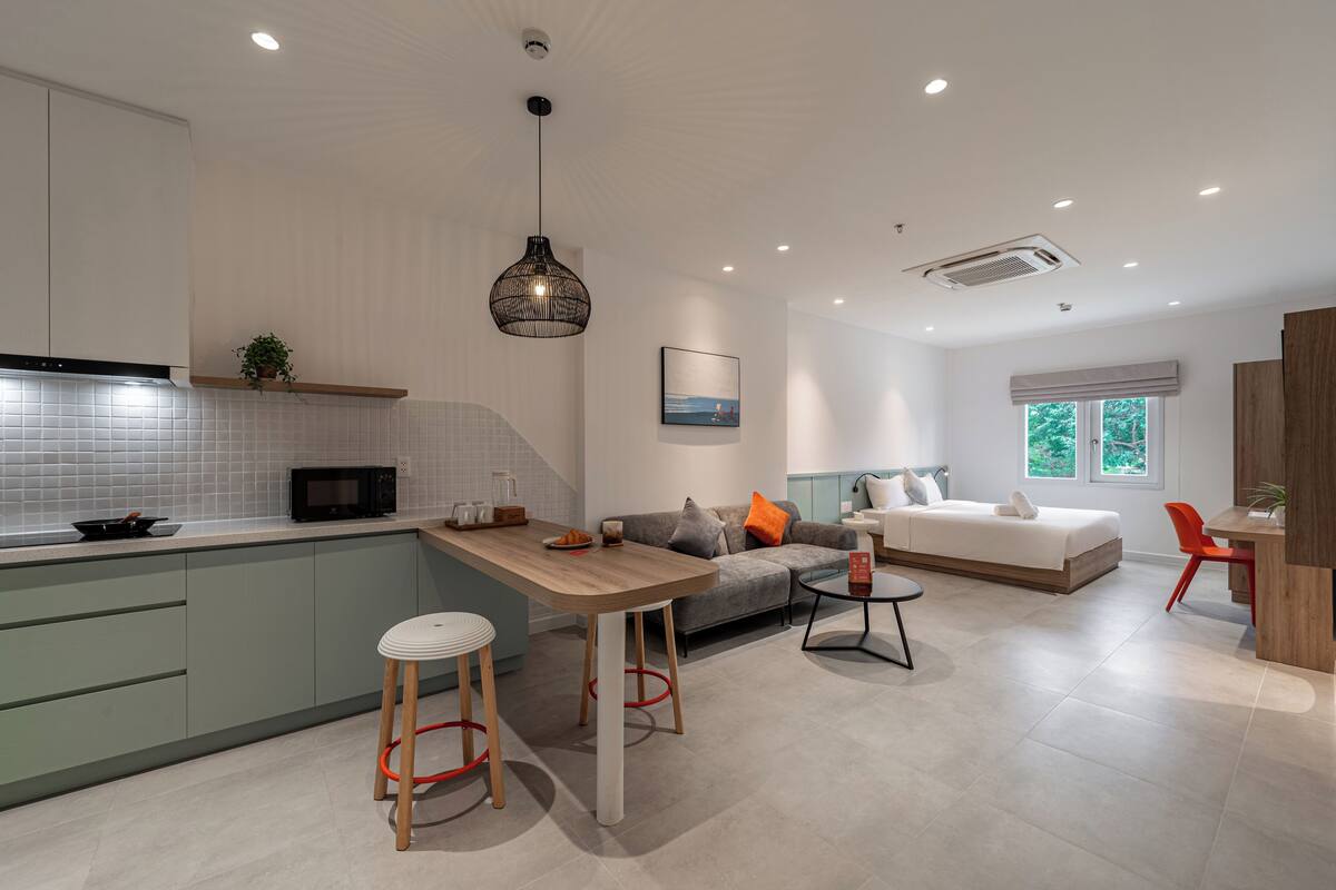 Eine moderne Küche mit Kochinsel, eine Essecke mit Hockern, ein Sofa und ein Bett in einem Schlafzimmer.