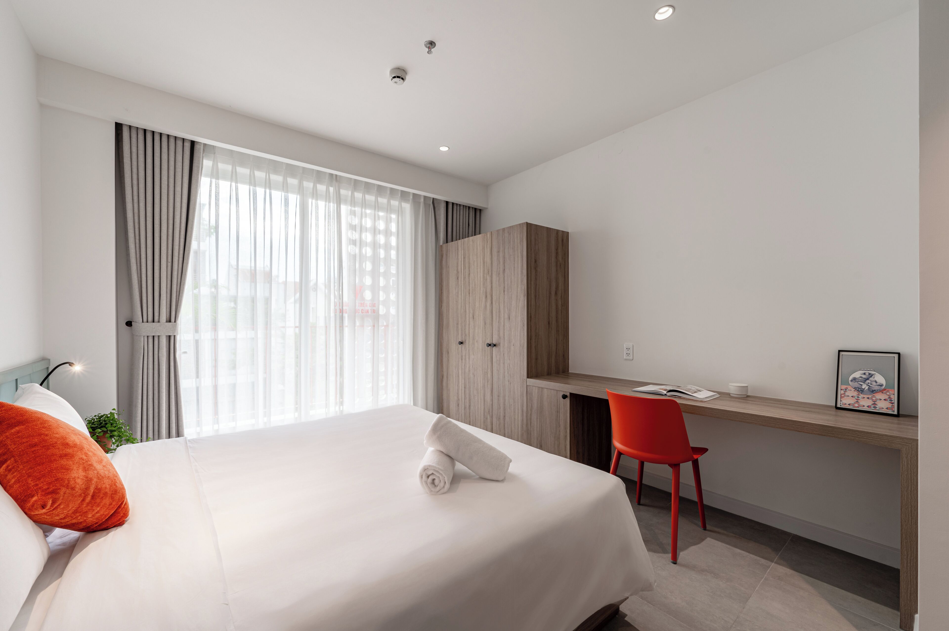 A hotel room with a bed, a desk, a chair, and a wardrobe.