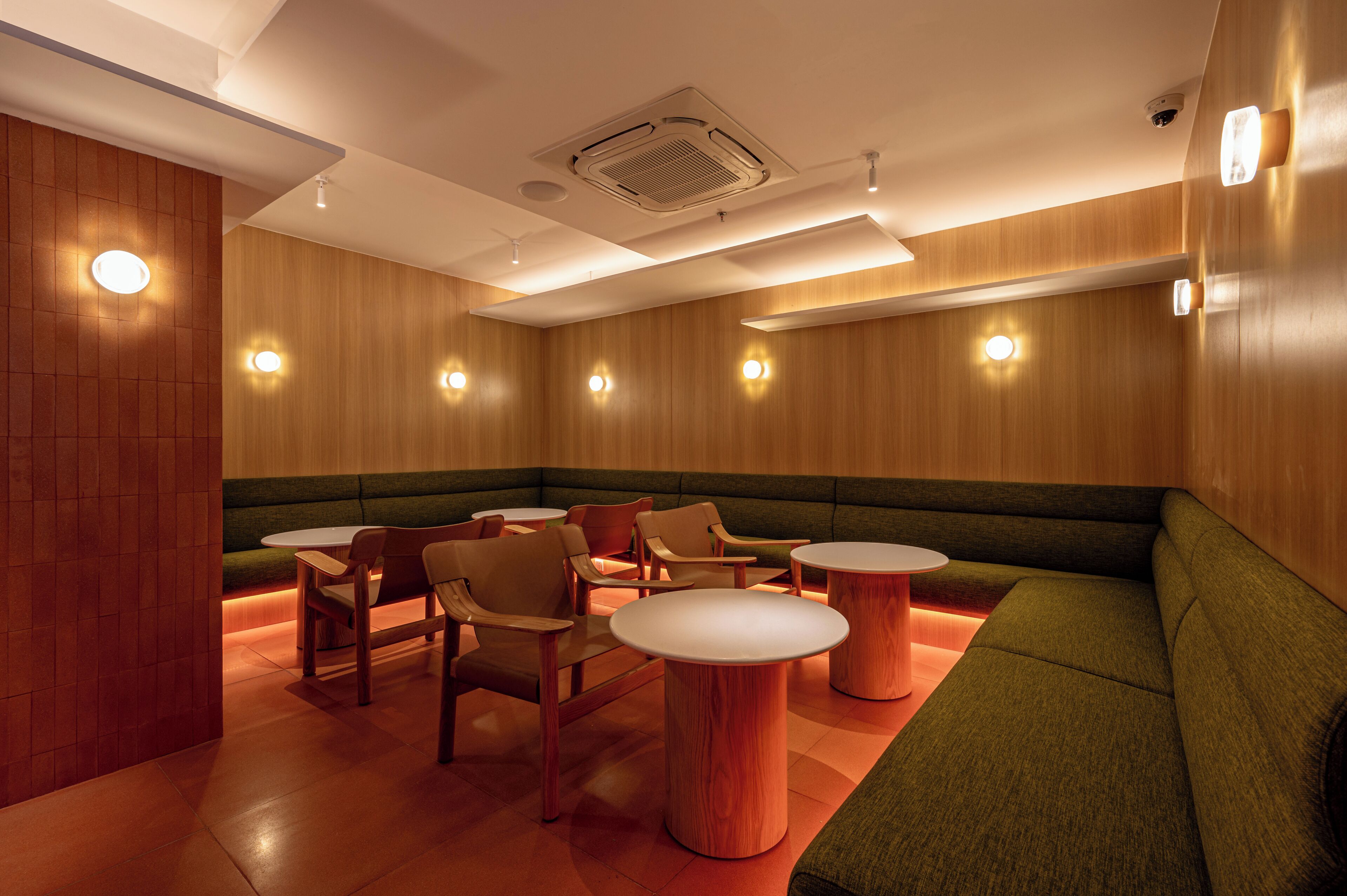 A modern lounge area with wooden panel walls, green cushioned seating, and round tables.