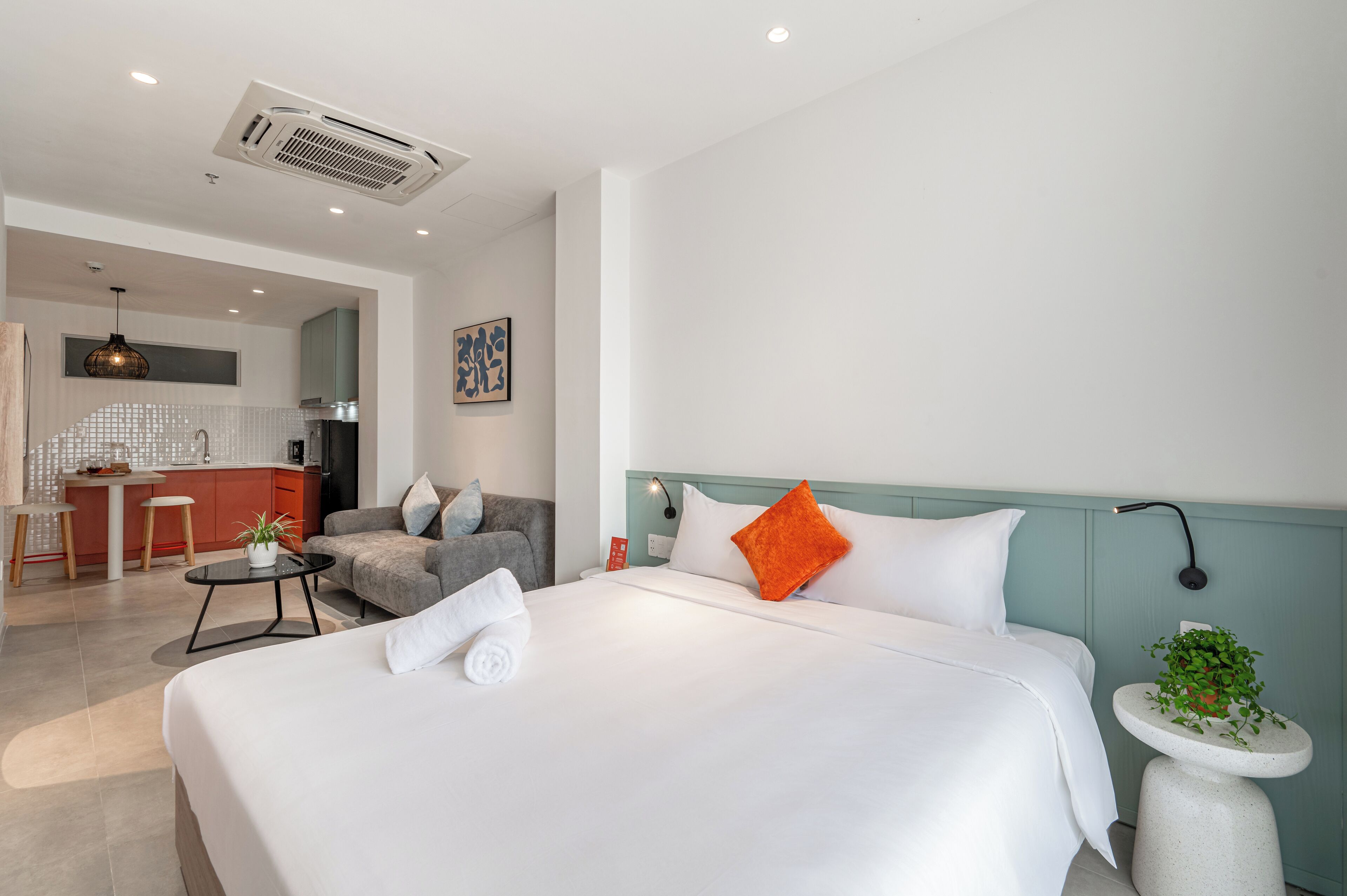 Una habitación de hotel con cama, una mesita redonda con una planta, un sofá, una zona de cocina y una mesa de comedor.