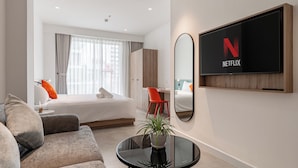 Una camera d'albergo moderna con un letto, una scrivania, una sedia, una TV e un divano.