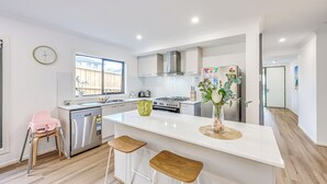 A modern kitchen with a central island, stainless steel appliances, and a window providing natural light. - StayAU Officer Newly 5BRM Homley Villa House (Officer)