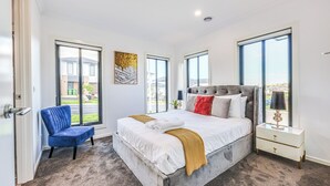 A modern bedroom with a large bed, a blue chair, and a nightstand. - StayAU Officer Newly 5BRM Homley Villa House (Officer)