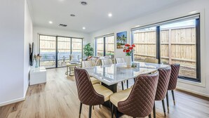 A spacious dining area with a large table and cushioned chairs, large windows with a view of a wooden fence, and a ceiling with recessed lighting. - StayAU Officer Newly 5BRM Homley Villa House (Officer)