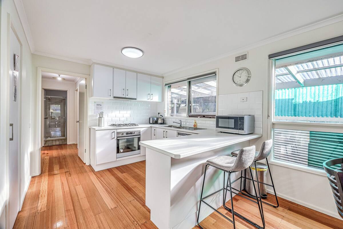 A modern kitchen with white cabinetry, a central island, a microwave, and a sink.