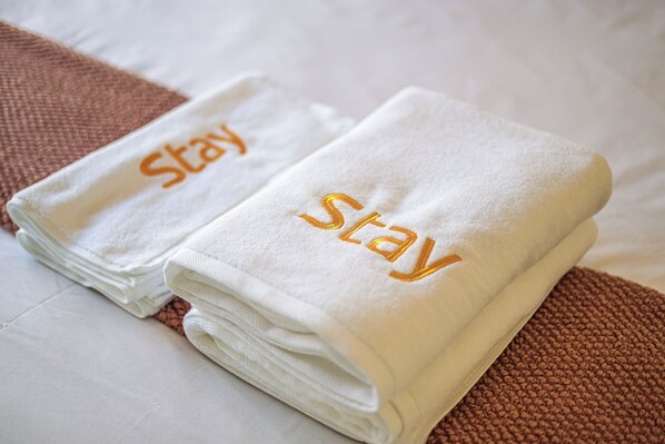 Two neatly folded white towels with the word "stay" embroidered in gold on them, placed on a bed with a brown textured bedspread. - StayAU Newly Modern Comforts 3BRM Home Cranbourne (Cranbourne)