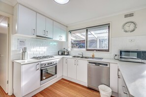 A modern kitchen with white cabinets, a built-in oven, a dishwasher, and a microwave. - StayAU Newly Modern Comforts 3BRM Home Cranbourne (Cranbourne)