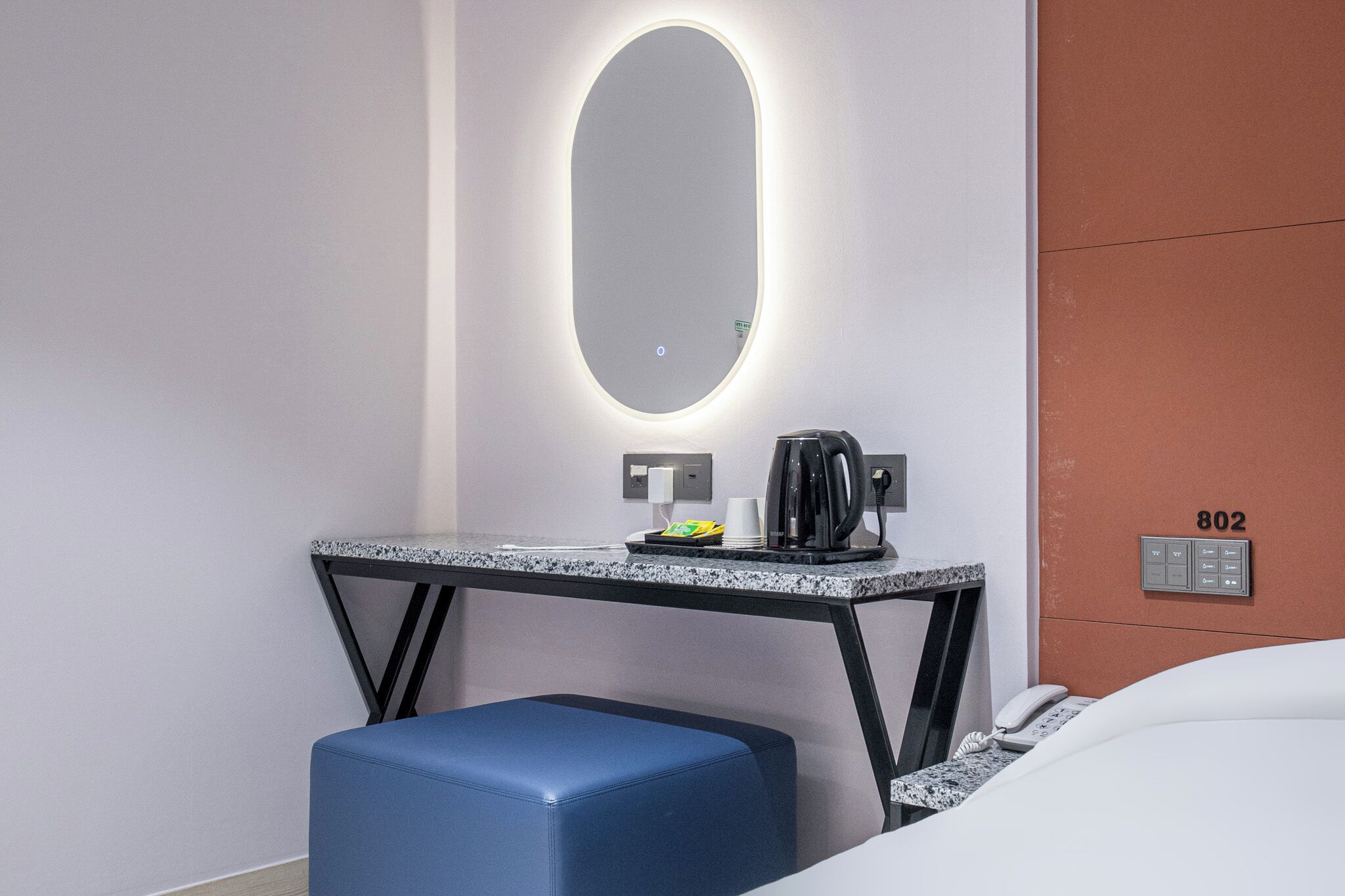 Habitación de hotel con cama, escritorio con cafetera, teléfono y espejo montado en la pared.