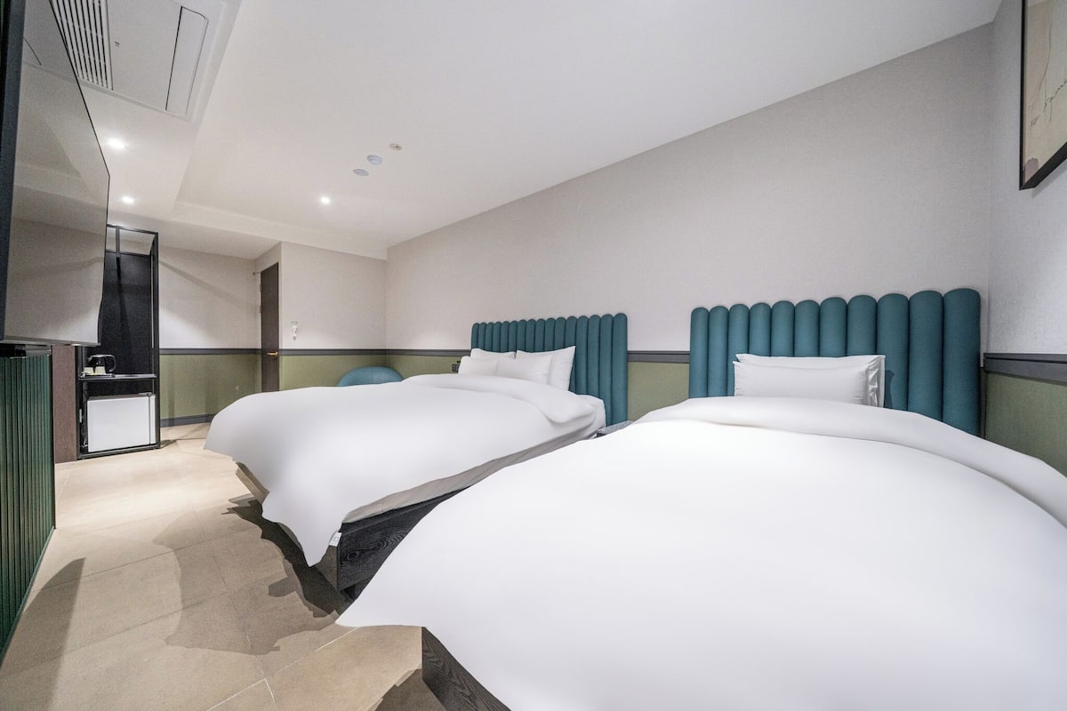 A hotel room with two beds, a small desk, and a kitchenette.