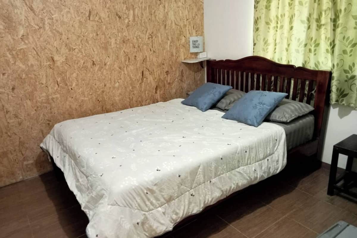 A single bed with a wooden headboard, a white quilted bedspread, and two pillows.