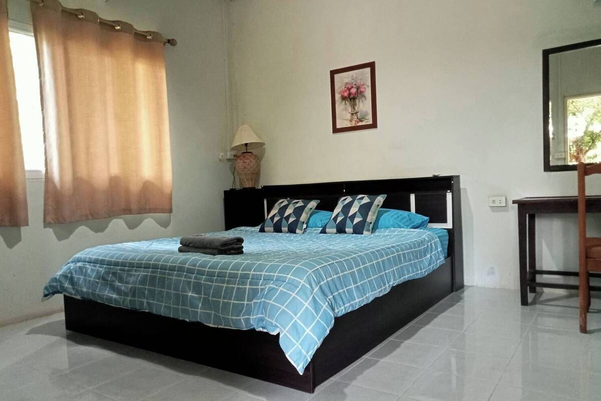 A bedroom with a bed, a nightstand, a lamp, a chair, and a framed picture on the wall.