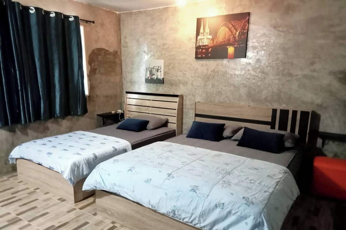 A bedroom with two beds, a nightstand, a wall-mounted picture, and a window with curtains.