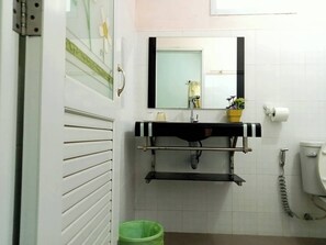 Een badkamer met een witte betegelde muur, een zwart-wit gestreepte wastafel, een spiegel, een toilet en een groene prullenbak.