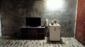 A room with a flat-screen TV on a wooden cabinet, a small refrigerator, and a wall-mounted air conditioner. - Ingna Resort (Chanuman)