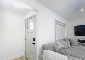 A modern living room with a grey sofa, a flat-screen TV mounted on the wall, and a white door with a window.