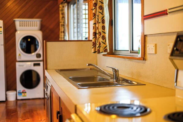 Cocina compacta con un lavamanos, dos lavadoras apiladas y una ventana con cortinas estampadas.