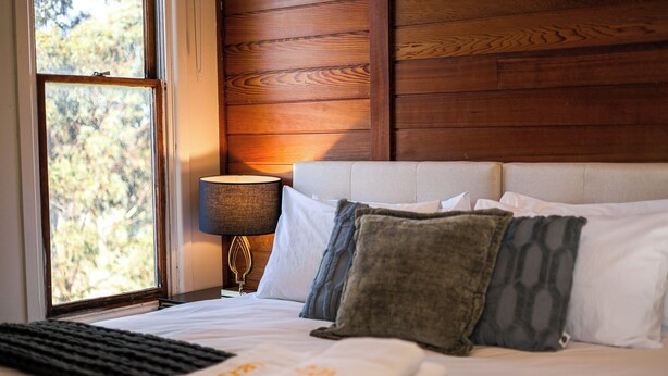 Ein Schlafzimmer mit einem Bett, Kissen, einer Lampe und einem Fenster mit Blick auf Bäume.
