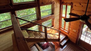A wooden interior with a spiral staircase, large windows, and a ceiling fan.