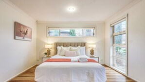 Ein ordentlich eingerichtetes Schlafzimmer mit einem großen Bett, zwei Nachttischen mit Lampen, einem Fenster mit Blick und einem gerahmten Bild an der Wand.