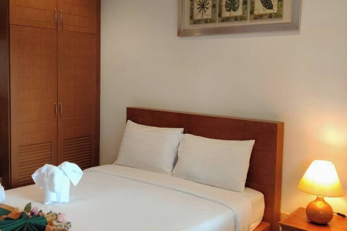 Un lit bien fait, avec du linge de lit blanc, une tête de lit en bois et une table de chevet avec une lampe.