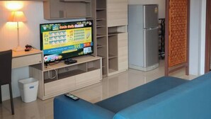 A modern living room with a blue sofa, a TV on a wooden stand, a refrigerator, and a wooden partition.