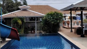 A swimming pool with a tiled deck, a slide, and a covered area with seating.
