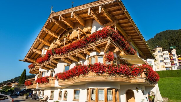 A traditional Alpine-style building with multiple balconies adorned with red flowers, a wooden facade, and a sloped roof. - Apartment with wellness & Premium Card (Wildschönau)