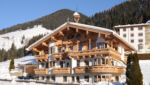 Eine große, mehrstöckige Holzhütte mit Balkonen, umgeben von schneebedeckten Bergen.