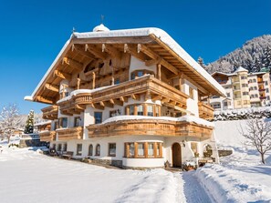 Een chalet met meerdere verdiepingen, houten balkons en een met sneeuw bedekte dak, gelegen in een besneeerd landschap.
