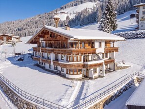Una chaleta de varios pisos con techo nevado, balcones de madera y base de piedra.