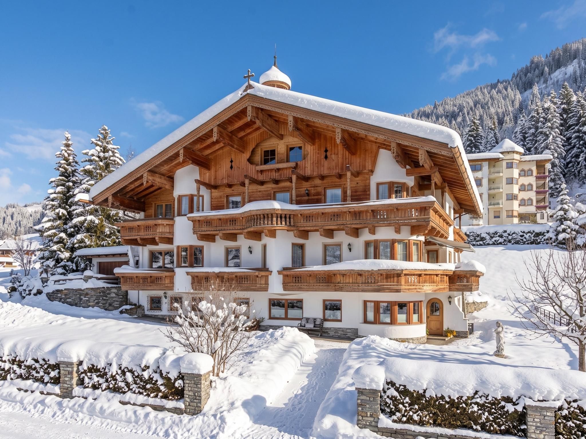 A multi-story wooden chalet with balconies, surrounded by snow-covered trees and a mountainous backdrop.