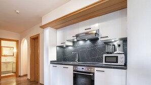 Cozinha moderna com armários brancos, painel de fundo de mármore preto, forno embutido e micro-ondas.