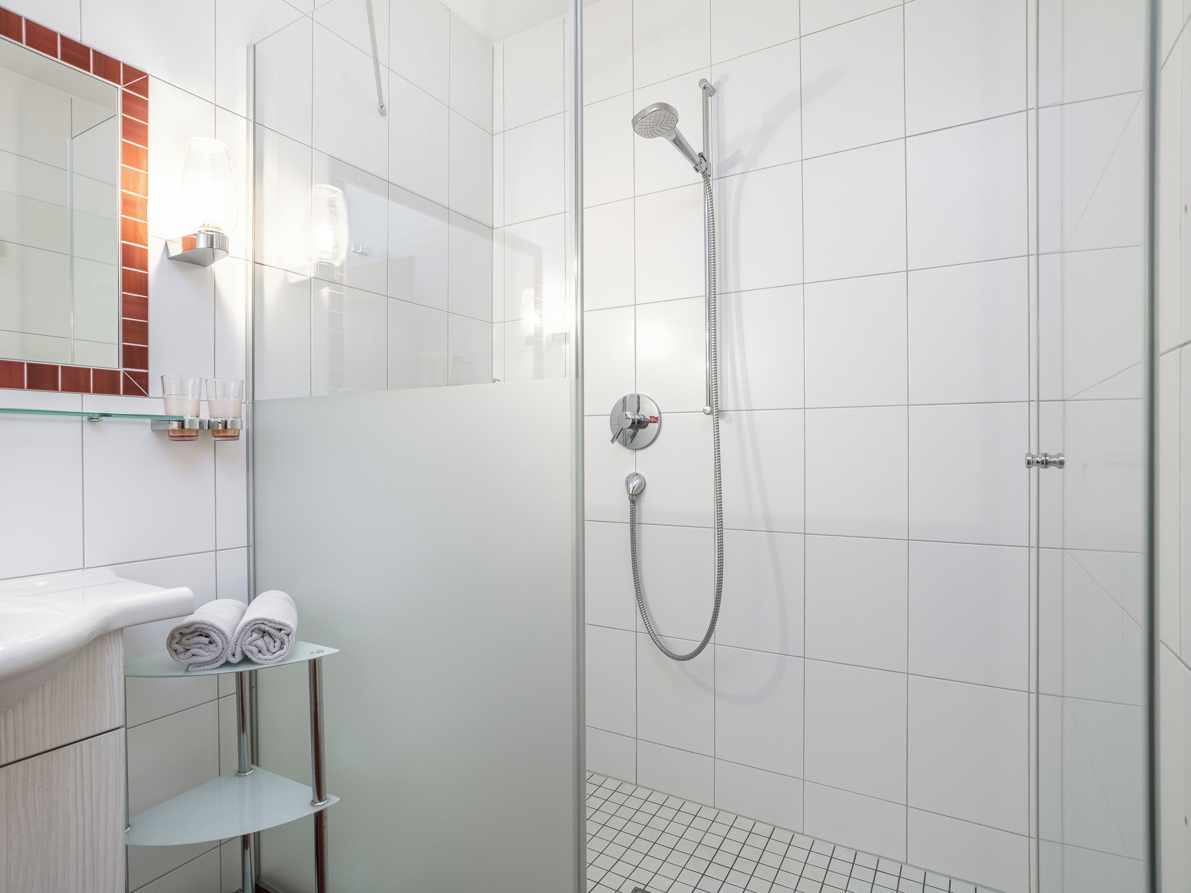 A modern bathroom with a glass shower enclosure, a white sink with a mirror, and a towel rack.
