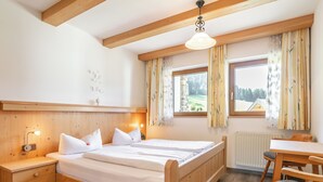 Un lit en bois avec du linge de lit blanc, une table de chevet, une chaise et une fenêtre avec des rideaux.